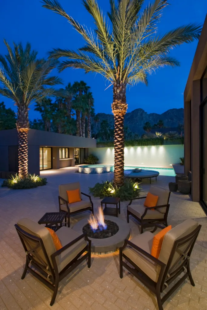 Hotel patio with fire pit surrounded by palm trees and outdoor chairs. 