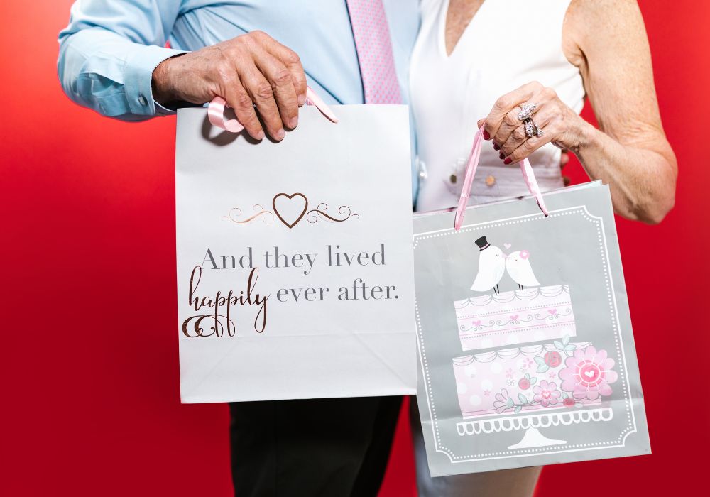 couples holding out paper bags with gifts on red background
