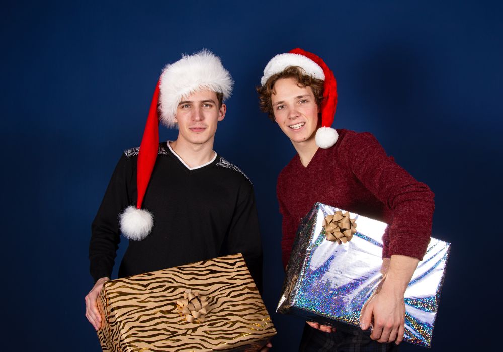 two college guys holding gifts while wearing santa hats