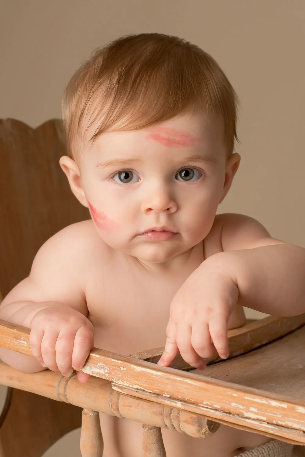 Photo of a baby in a high chair with lipstick kisses on their face.