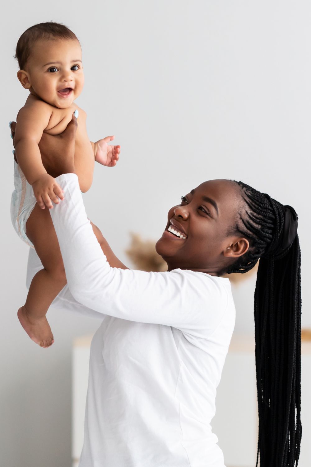 a photo of a woman holding a baby up in the air while smiling
