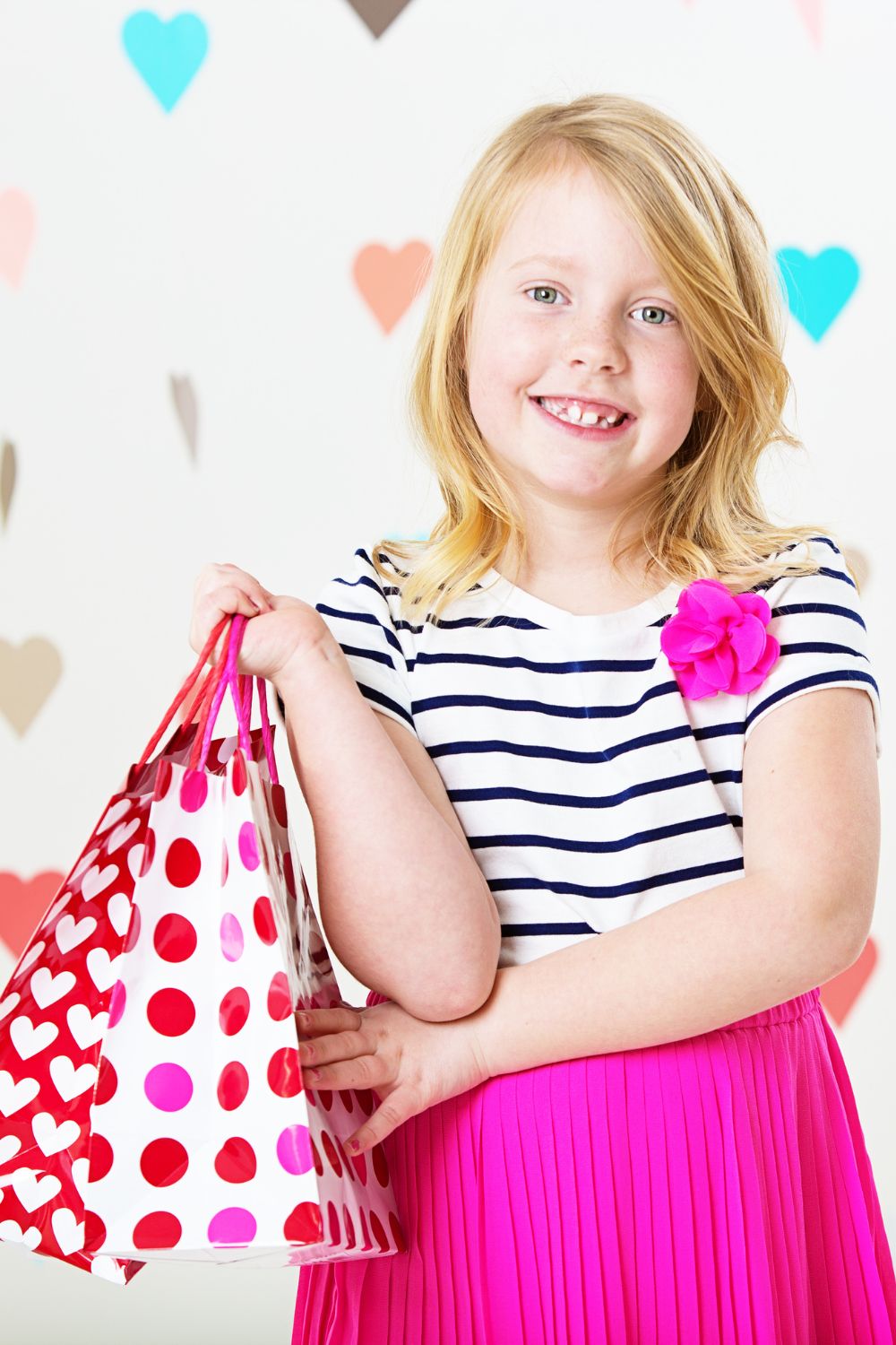 little girl holding shopping bags that are Valentine themed.