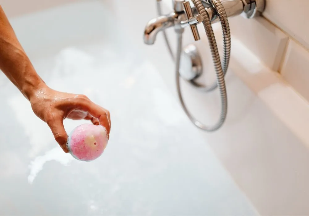 person holding a bath bomb on a bath tub